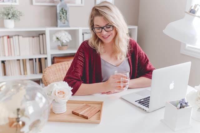 Woman wearing a red cardigan sitting in front of a laptop and looking at a bouquet of flowers in front of her